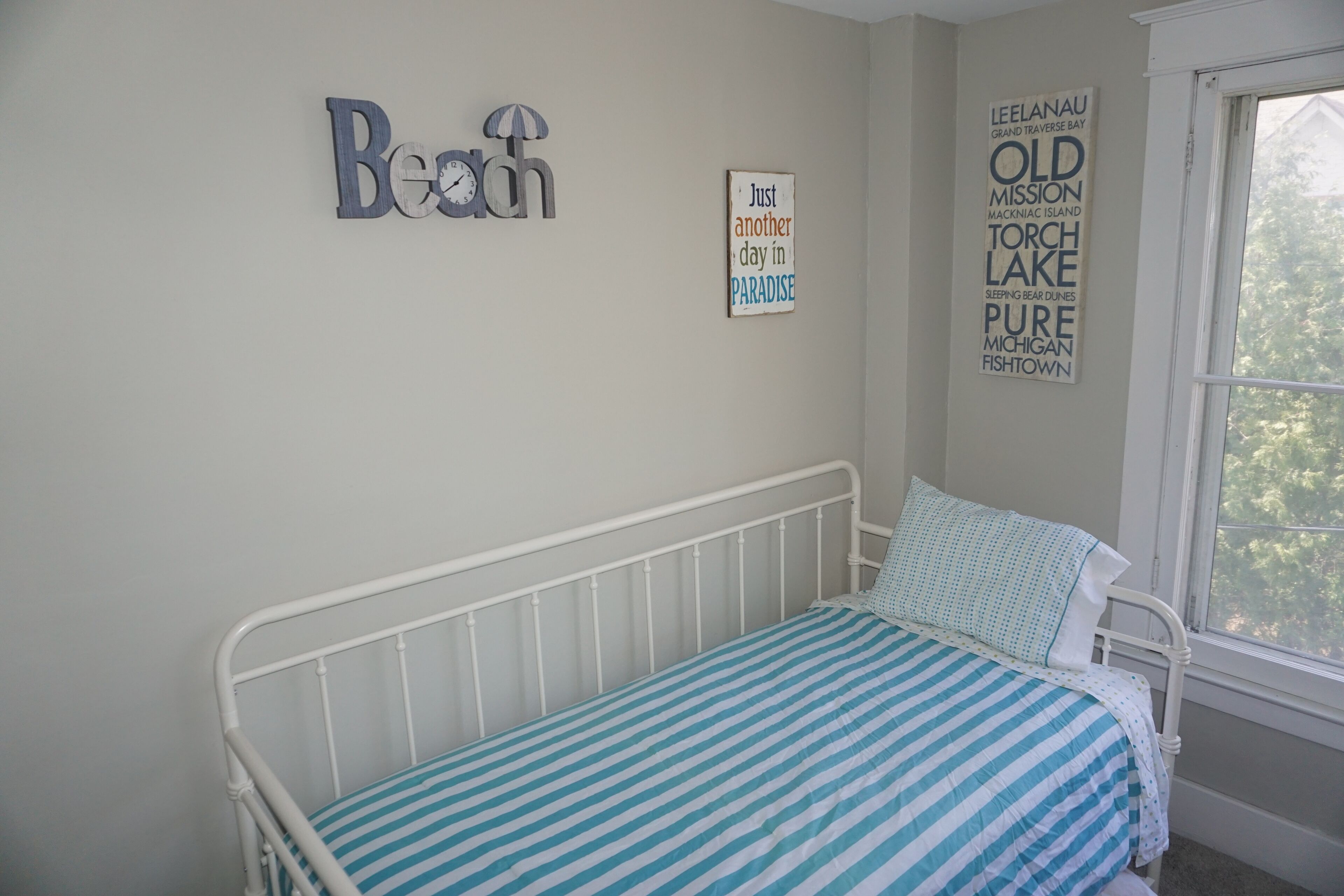 A bedroom with a bed, a window, and wall decorations including a clock and a sign with text.