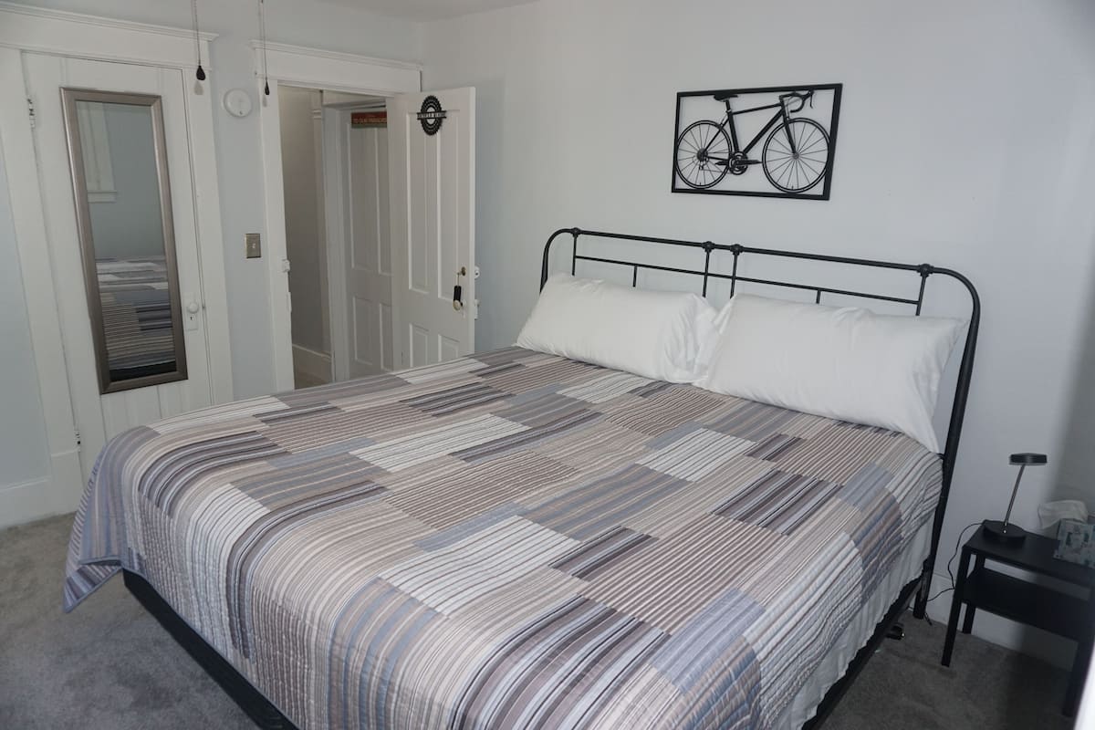 A bedroom with a bed, a wall-mounted bicycle artwork, and a door with a mirror.