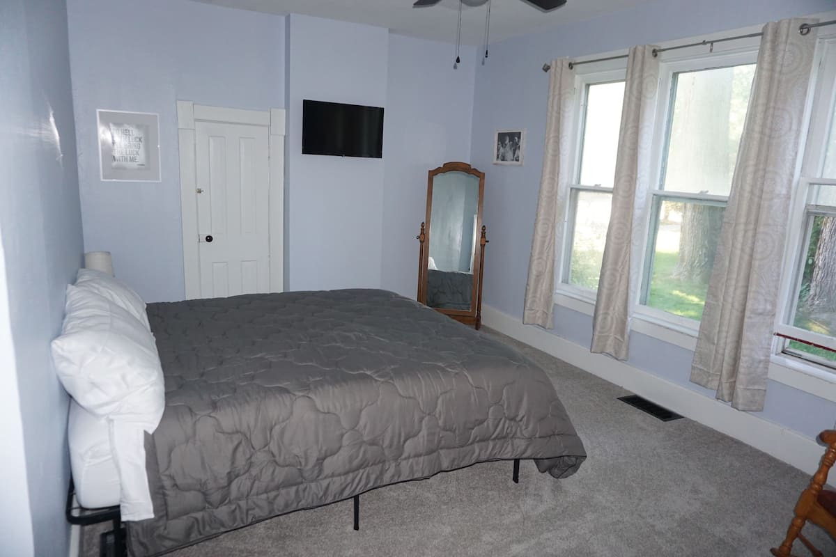 A bedroom with a bed, a mirror, a television, and a window with curtains.