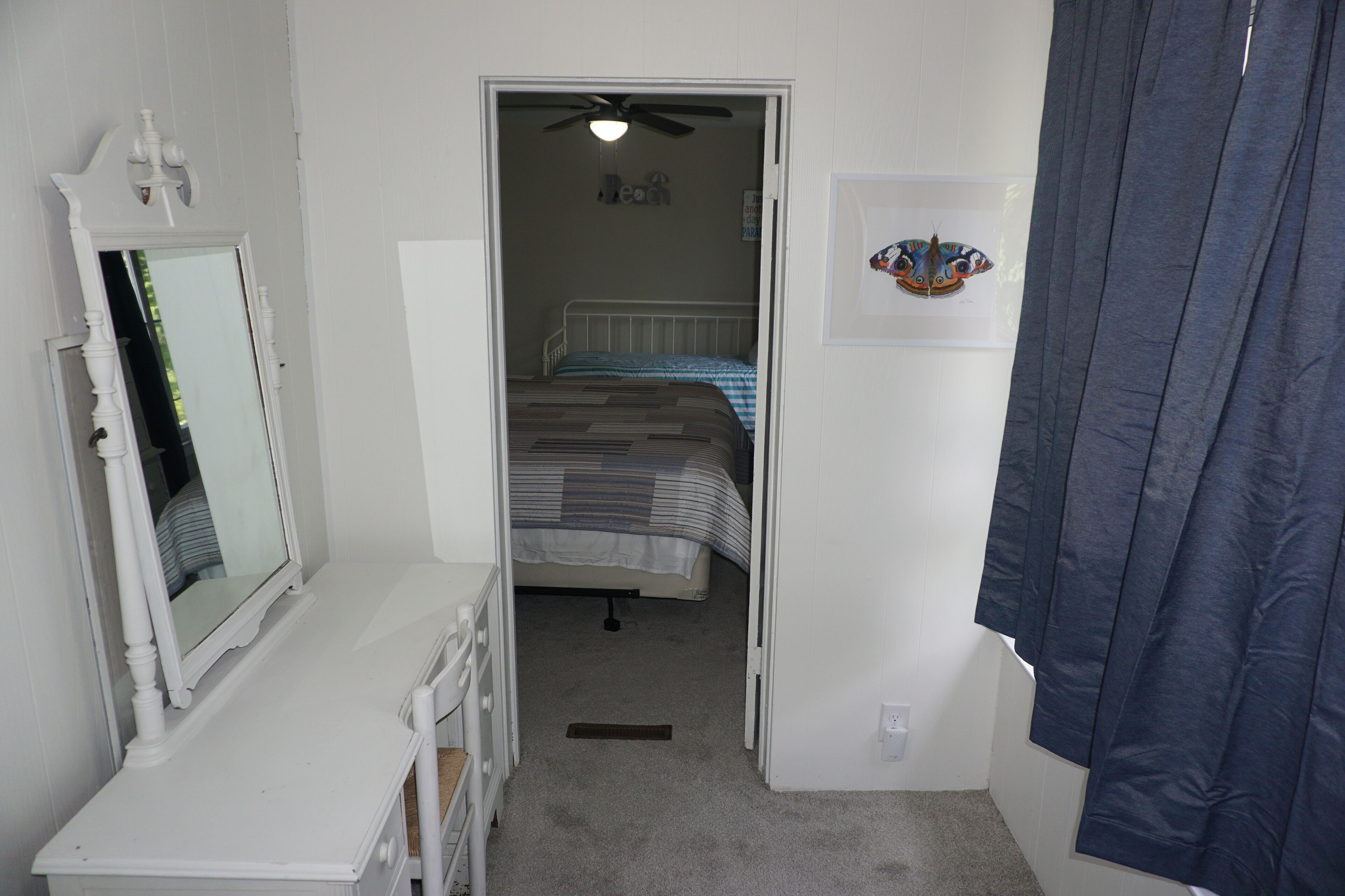 A bedroom with a bed, a dresser, a mirror, a ceiling fan, and a door leading to another room.