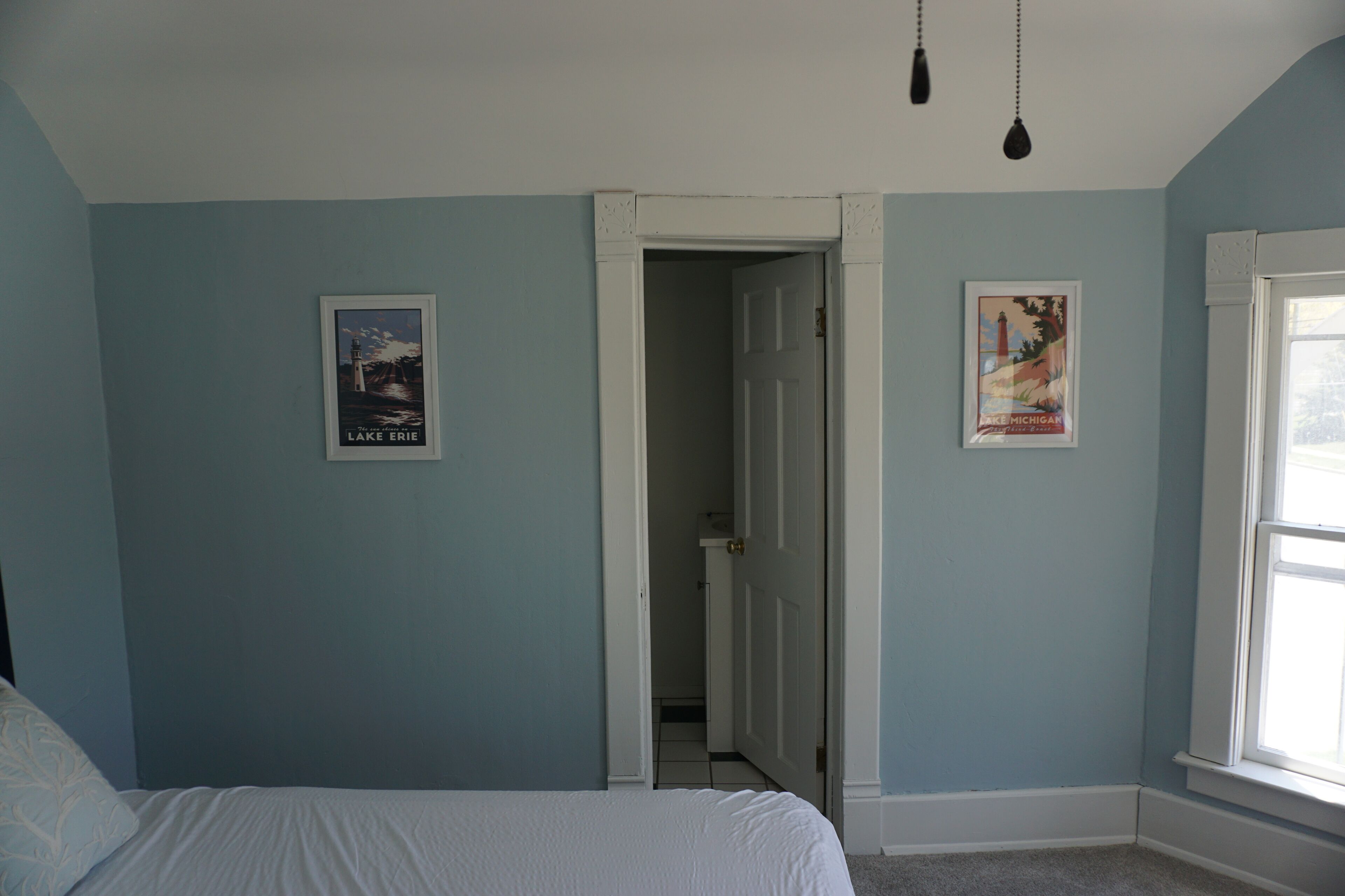 A bedroom with a bed, a door leading to a bathroom, and two posters on the wall.