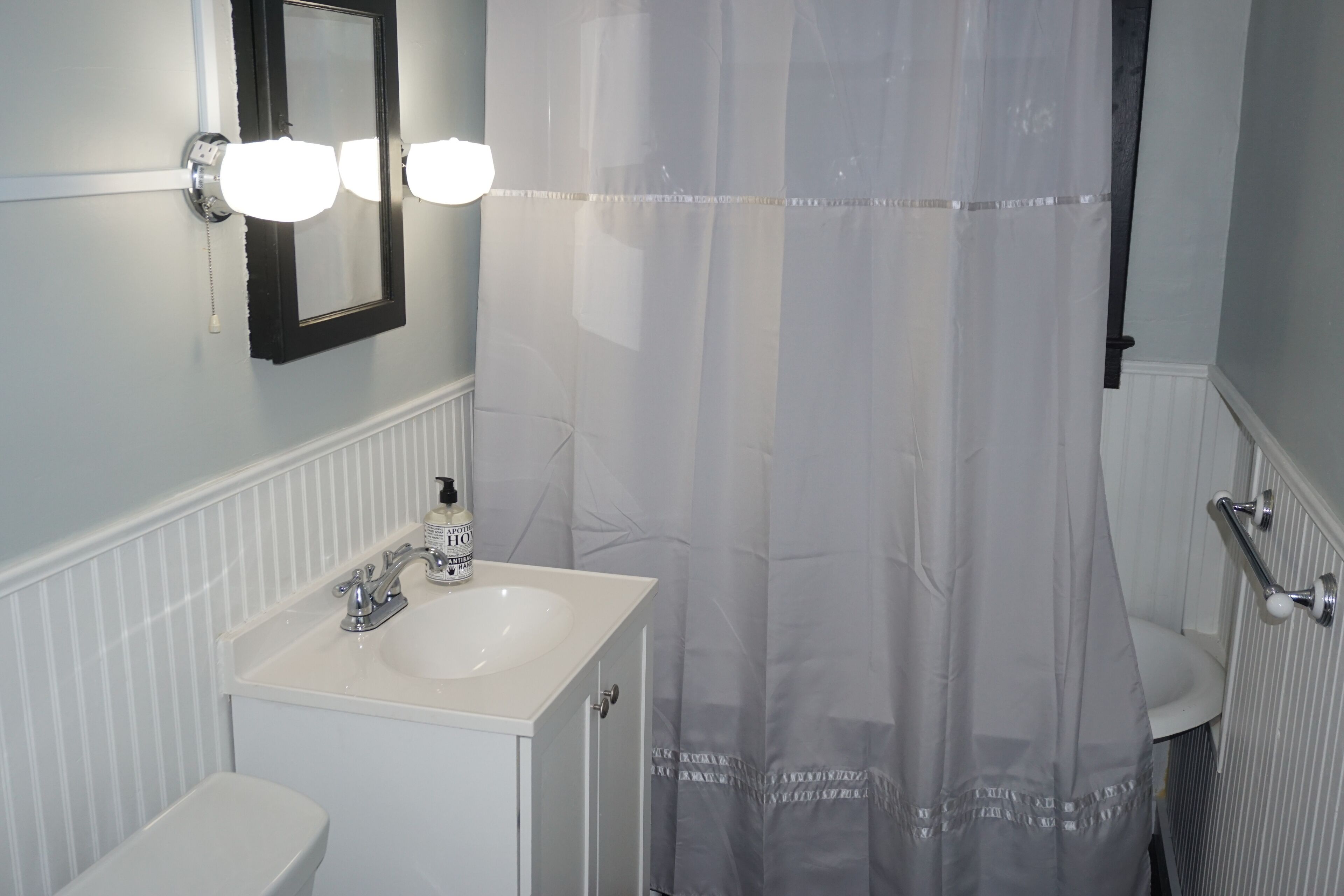 Une salle de bain avec un lavabo blanc, un miroir et un rideau de douche.