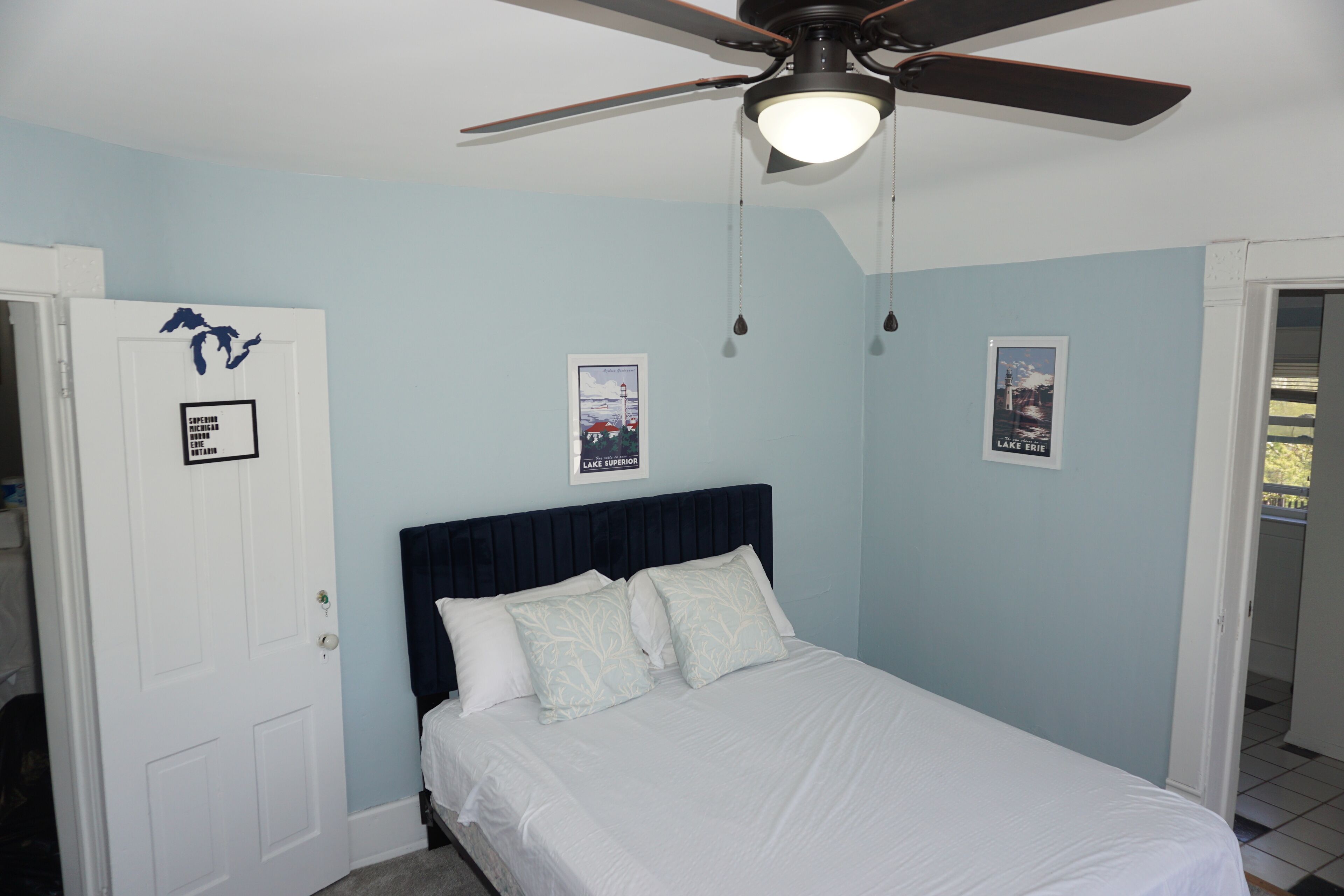 A bedroom with a bed, a ceiling fan, and two framed pictures on the wall.