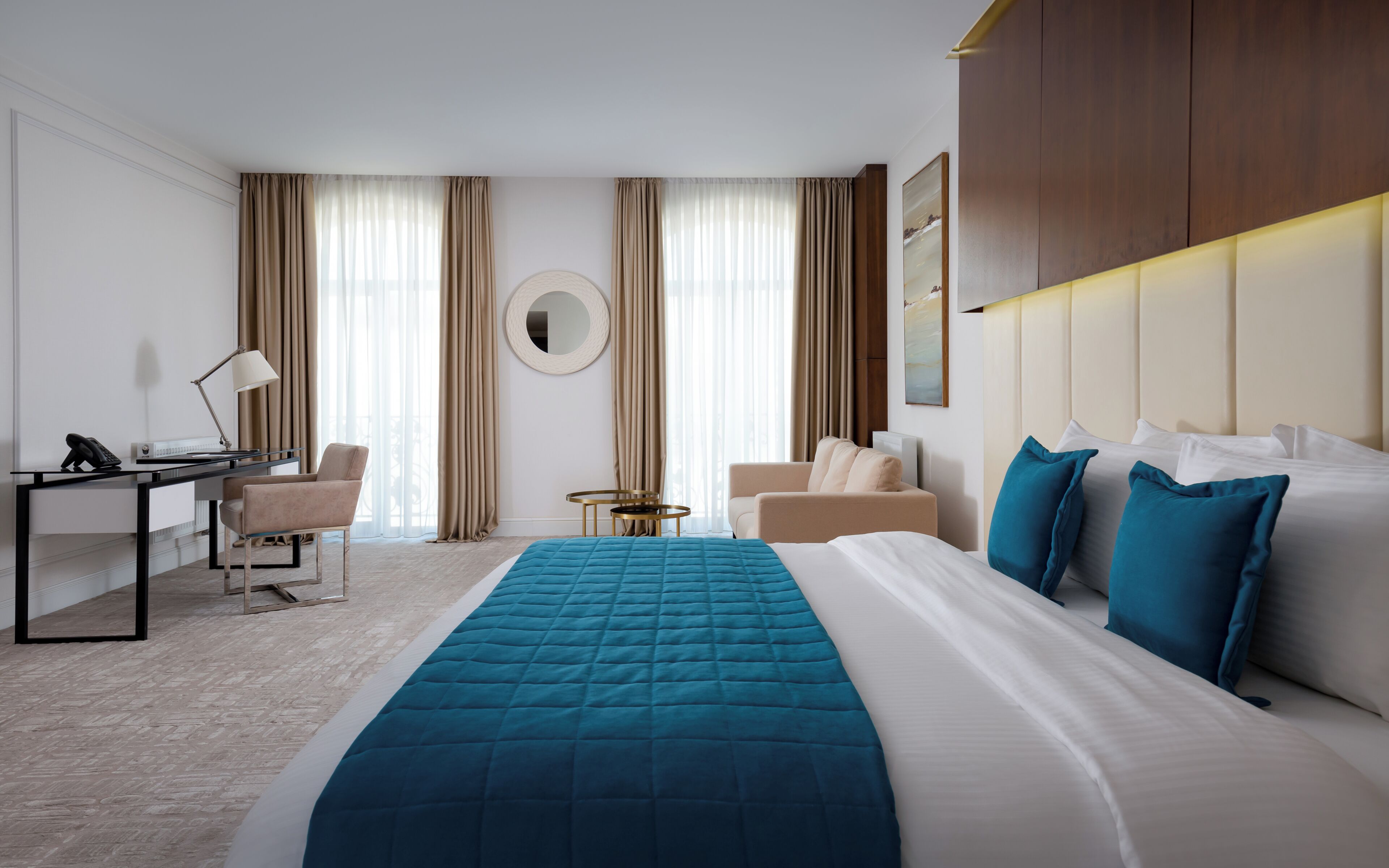 A hotel room with a bed, a desk, a chair, a round mirror, and a small table.