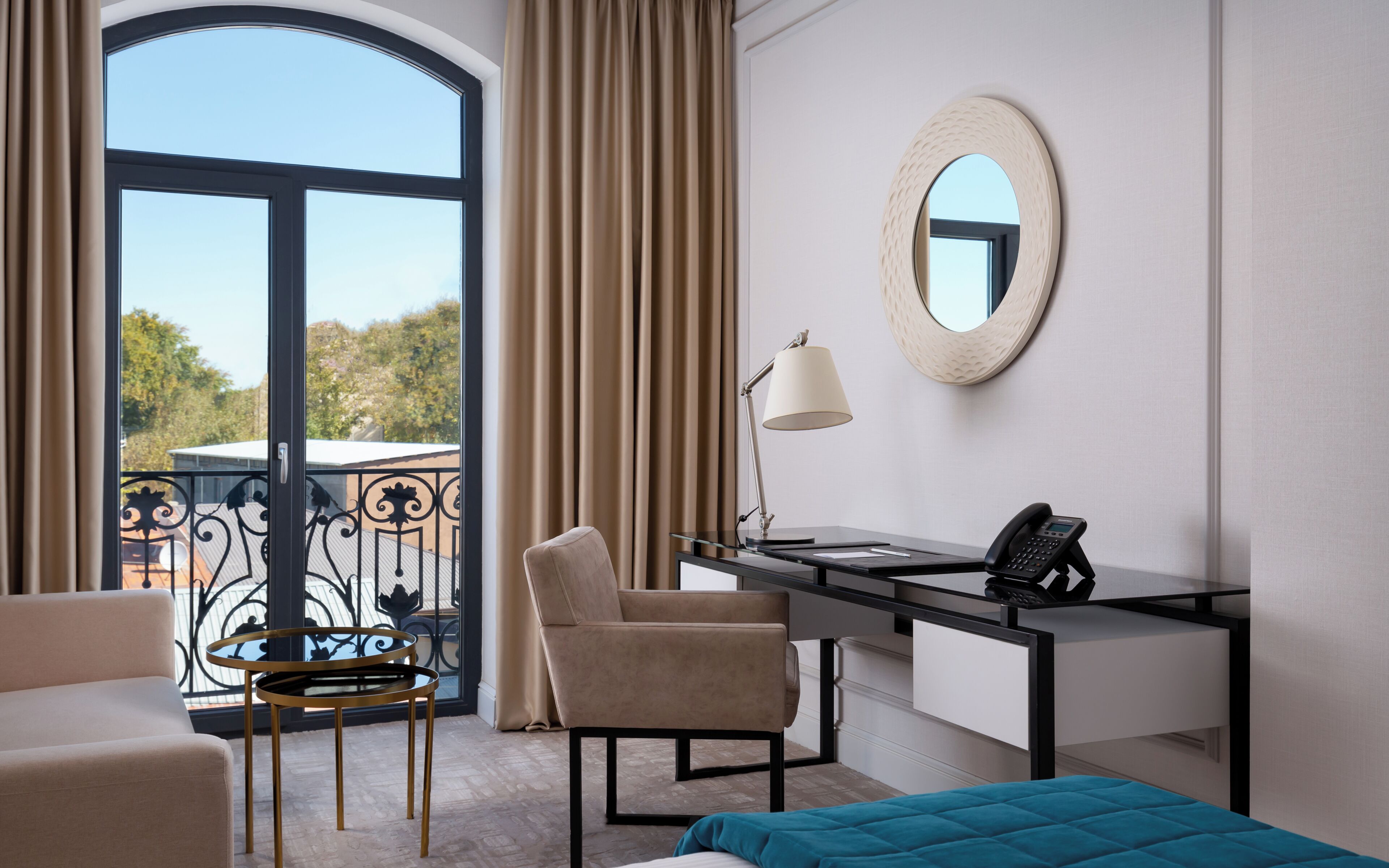 A hotel room with a desk, chair, bed, and a view through a large window.