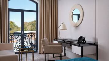 A hotel room with a desk, chair, bed, and a view through a large window.