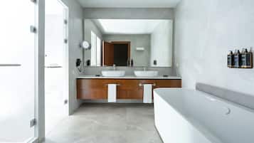Un baño moderno con dos lavamanos, un espejo grande, una bañera y un tocador con toallero.