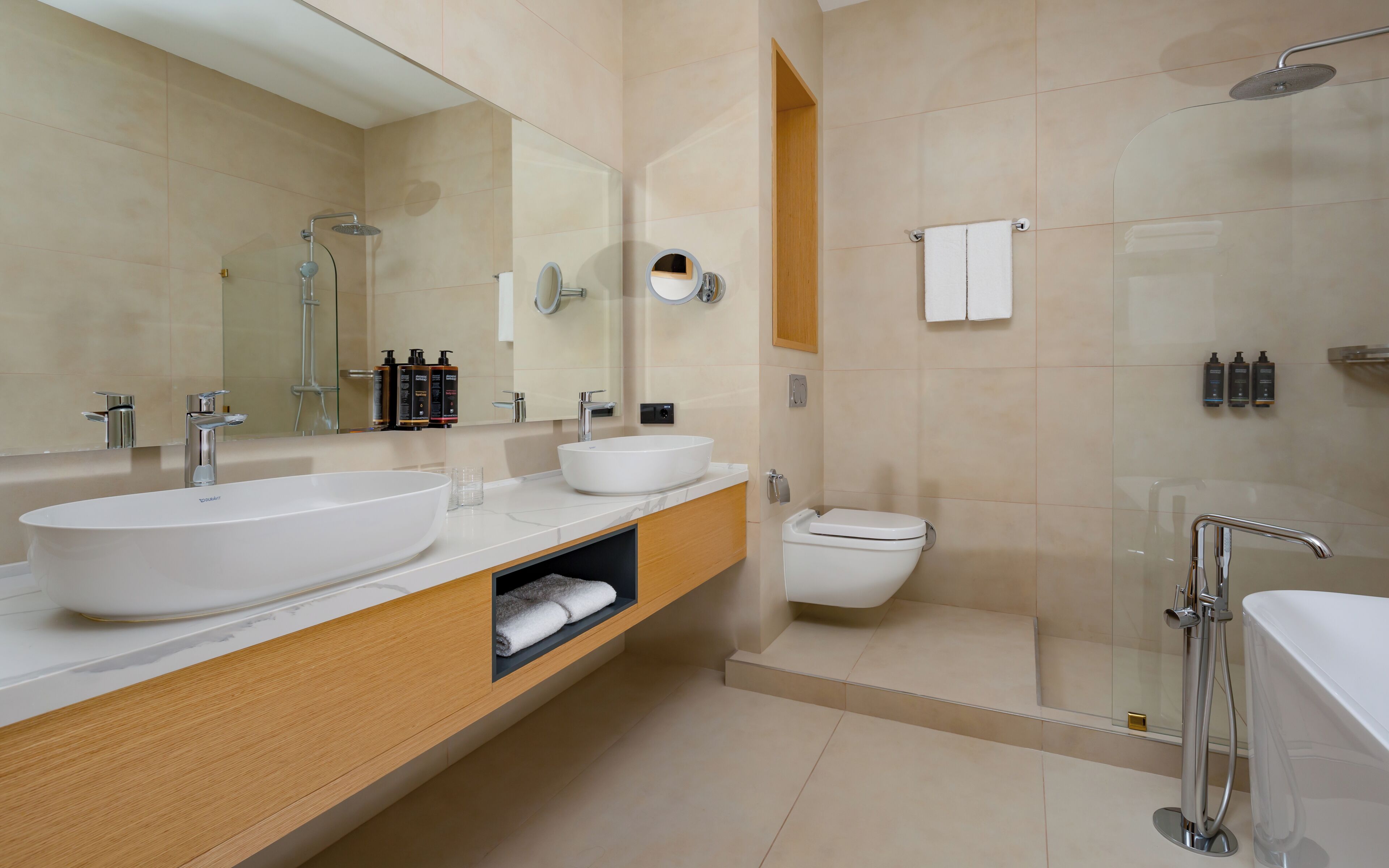 Een moderne badkamer met een dubbele wastafel, toilet, douche en een grote spiegel.