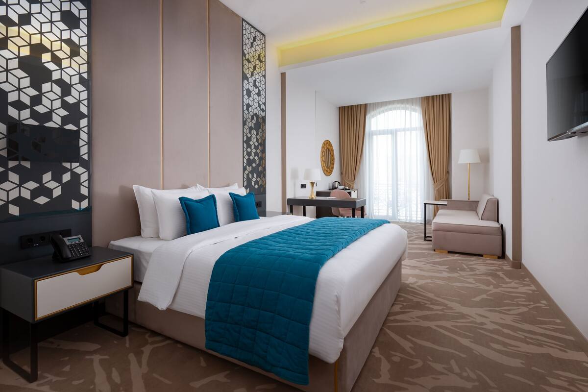 A hotel room with a large bed, a desk, a chair, and a TV.