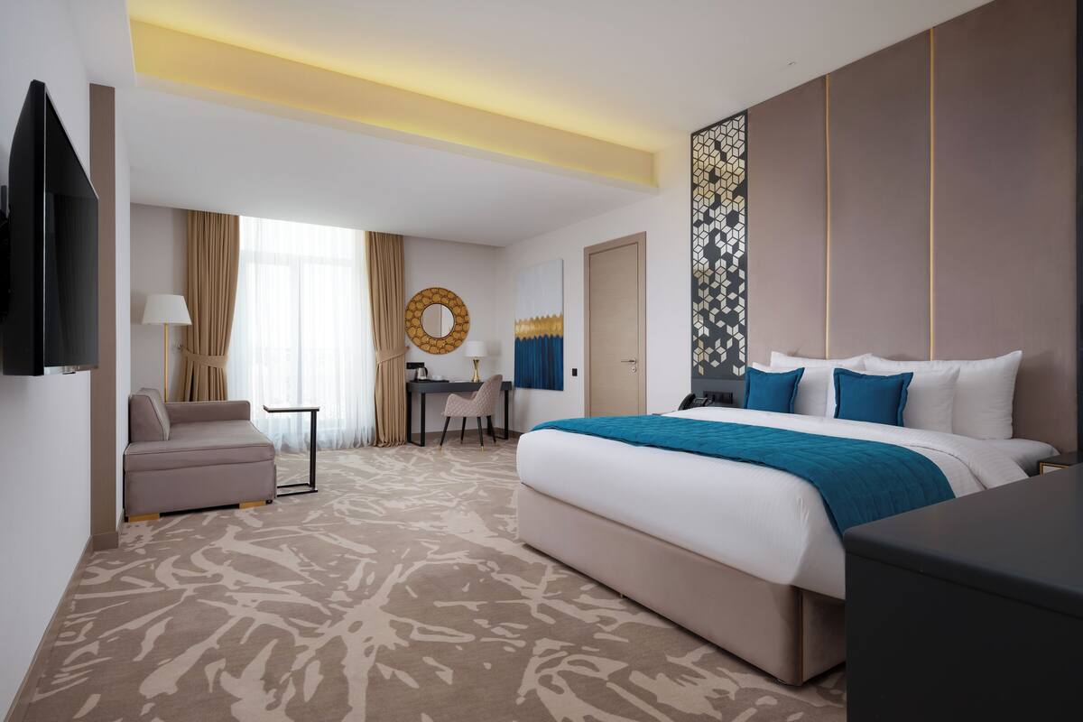 A modern hotel room with a large bed, a desk, a chair, and a TV.
