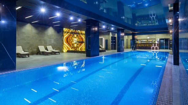 A modern indoor swimming pool with clear lanes, lounge chairs, and a bar area. - Mercure Tashkent South (Tashkent)