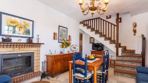 Un salon avec une cheminée, une table à manger avec des chaises, un escalier et un lustre.