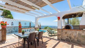 Une terrasse avec une table et des chaises, une piscine et un four en pierre.