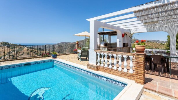 Une piscine offrant une vue dégagée sur la mer, un espace barbecue et une pergola avec des sièges d’extérieur.