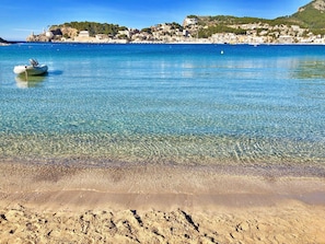 Une plage côtière avec une eau claire, un bateau et une ville en arrière-plan.