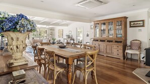 A spacious dining area with a wooden table and chairs, a large vase with flowers, and a wooden cabinet with glass doors. - Hampshire Farmhouse - beautifully appointed home in WA's Southern Forests (Upper Warren)