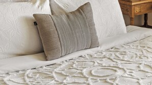 Una cama con cabecera trenzada, múltiples almohadas y una colcha blanca con textura.