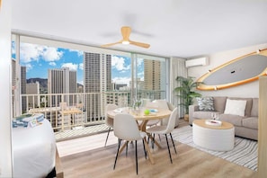 Un salon moderne comprenant un coin repas, de grandes fenêtres, un ventilateur de plafond et une vue sur les immeubles de la ville.