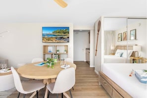 Ein modernes Hotelzimmer mit Bett, Essbereich mit Tisch und Stühlen, kleiner Küche und Bad.