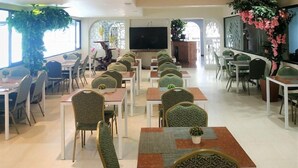 Un grand espace dédié à la salle à manger, avec plusieurs tables et chaises, un écran de télévision et des plantes décoratives.