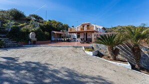 Ein zweistöckiges Haus mit Terrasse, Steinmauern und einem kleinen Schrein.