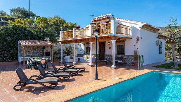 Ein zweigeschossiges Haus mit Swimmingpool, Sitzgelegenheiten im Freien und einer Grillstelle aus Stein.