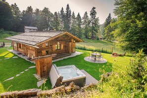 Une cabane en bois dotée d’un jacuzzi, entourée d’une pelouse bien entretenue et d’arbres.