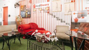 A hotel lobby with a red sofa, a beige armchair, and a glass coffee table. There are clocks on the wall and a RedDoorz sign.