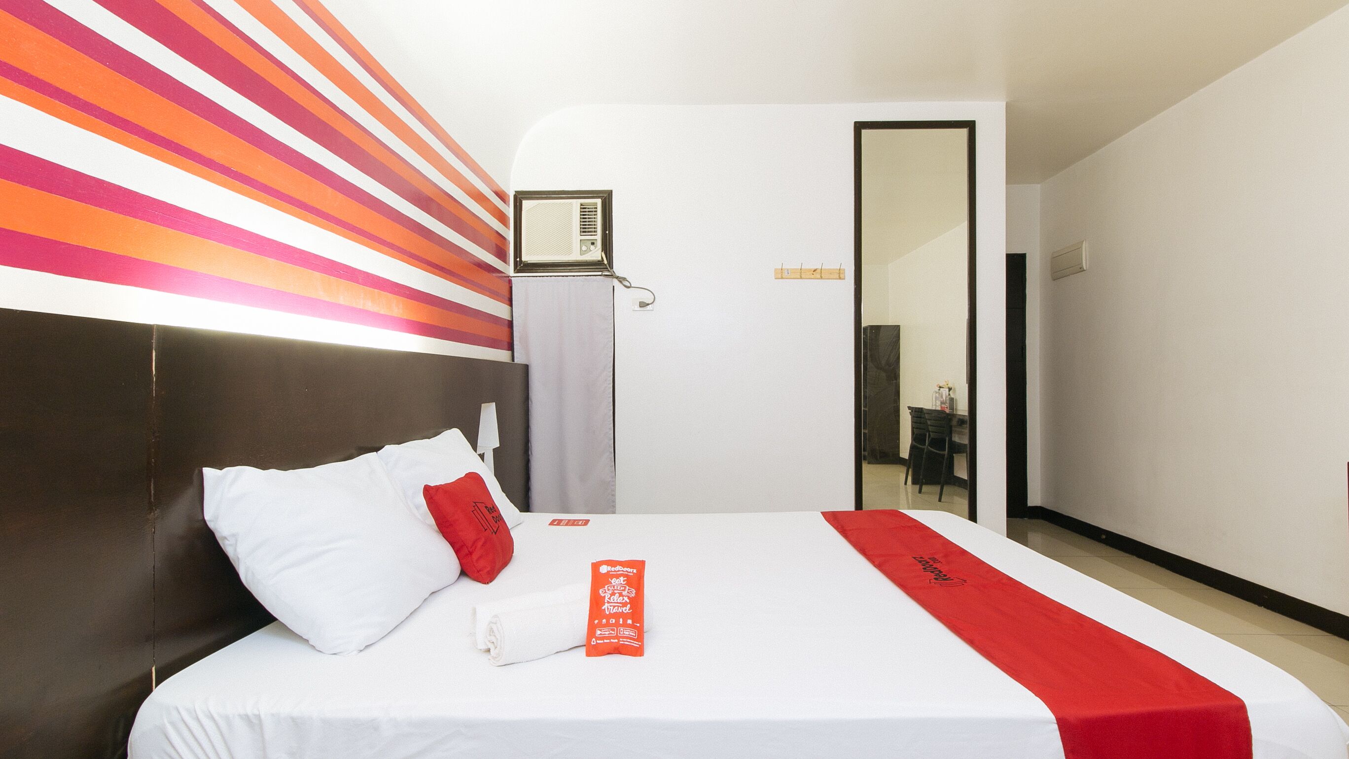 A hotel room with a bed, a headboard, a wall with a striped pattern, a window, and a door.
