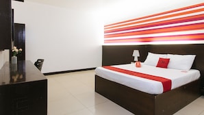 A hotel room with a bed, a bedside table, a lamp, and a wall with a striped pattern.