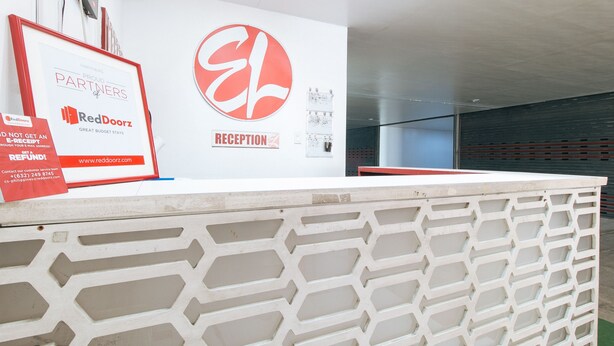 A reception desk with a RedDoorz sign, a reception area, and a wall-mounted light switch.