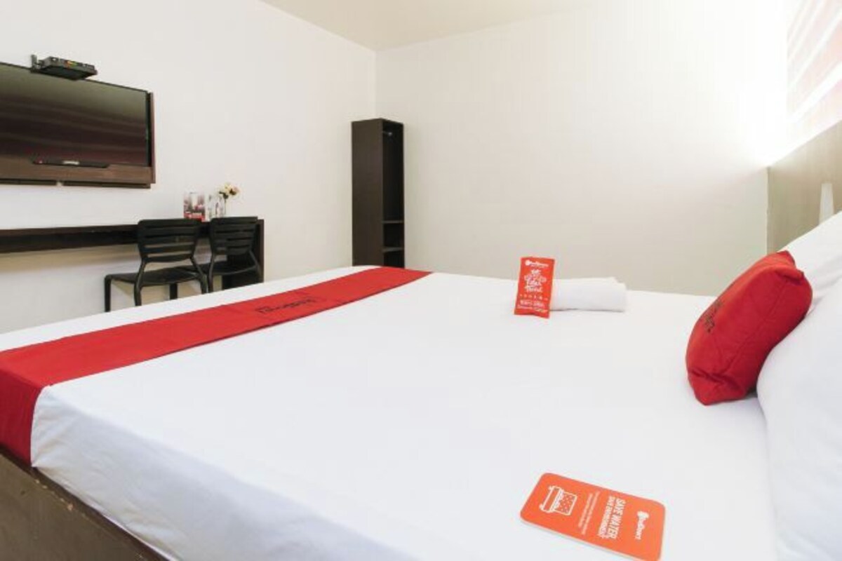 Una habitación de hotel con cama, escritorio, silla, televisor y estantería.