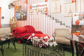Una habitación con un sofá rojo, un sillón beige, una mesa de centro de vidrio y una pared a rayas rojas y blancas con la marca RedDoorz.
