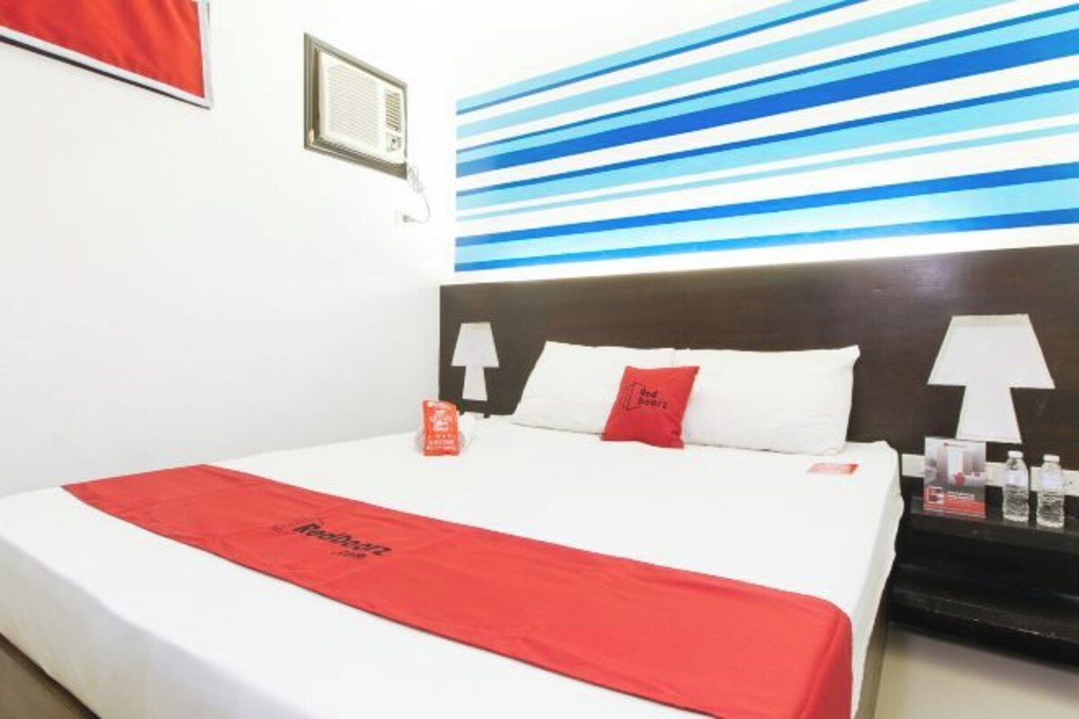 Una habitación de hotel con una cama, un edredón rojo, una almohada blanca y una pared con rayas azules.