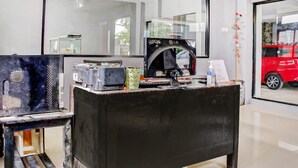 A reception desk with a mirror, a coffee machine, and a red car visible through the window. - Super OYO 3903 Sweethome Syariah Guesthouse (Banjarbaru)