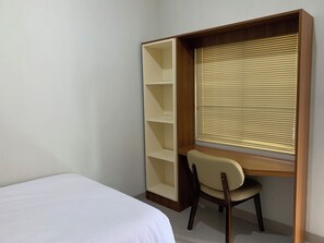 Une chambre à coucher avec un lit, un bureau avec une chaise et une fenêtre avec des stores.