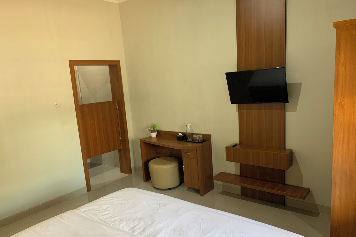A hotel room with a bed, a desk, a chair, a television mounted on the wall, and a wooden cabinet.