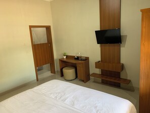 A hotel room with a bed, a desk, a chair, a television mounted on the wall, and a wooden cabinet.