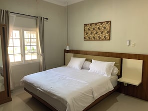 Habitación de hotel con una cama grande, una mesita de noche, una obra de arte en la pared y una ventana con cortinas.