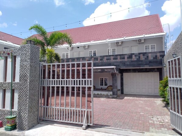 A gated entrance to a building with a red roof, a brick driveway, and a white garage door.