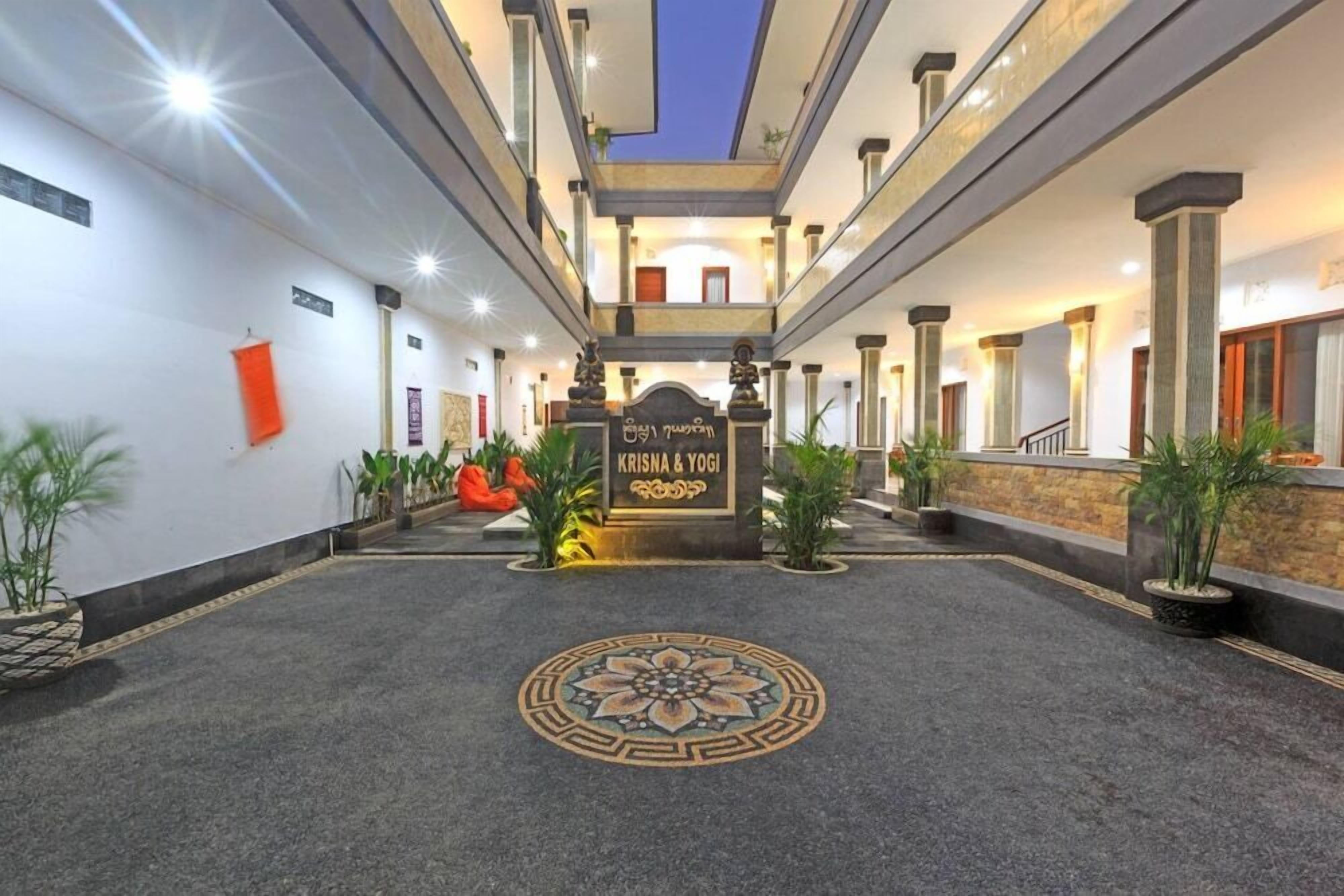 Un vestíbulo de hotel con un diseño decorativo en el suelo, un letrero que dice "KRISNA & YOGI" y una escalera que sube a niveles superiores.