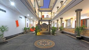 Un hall d’hôtel avec un motif décoratif central sur le sol, une enseigne indiquant « KRISNA & YOGI » et un escalier menant aux étages supérieurs.