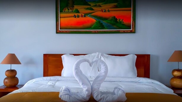 Une chambre d’hôtel avec un lit, deux lampes de chevet, un tableau au mur et deux serviettes en forme de cygne posées sur le lit.