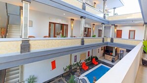 Un hôtel à plusieurs niveaux, avec un espace intérieur comprenant une piscine centrale, des balcons et un escalier.