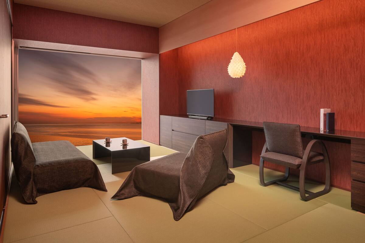 Een moderne kamer met tatami matten, een bank, een stoel, een kleine tafel en een televisie op een houten kast.