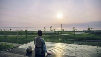 Una persona sentada en un balcón con vista al agua, bajo un cielo despejado.