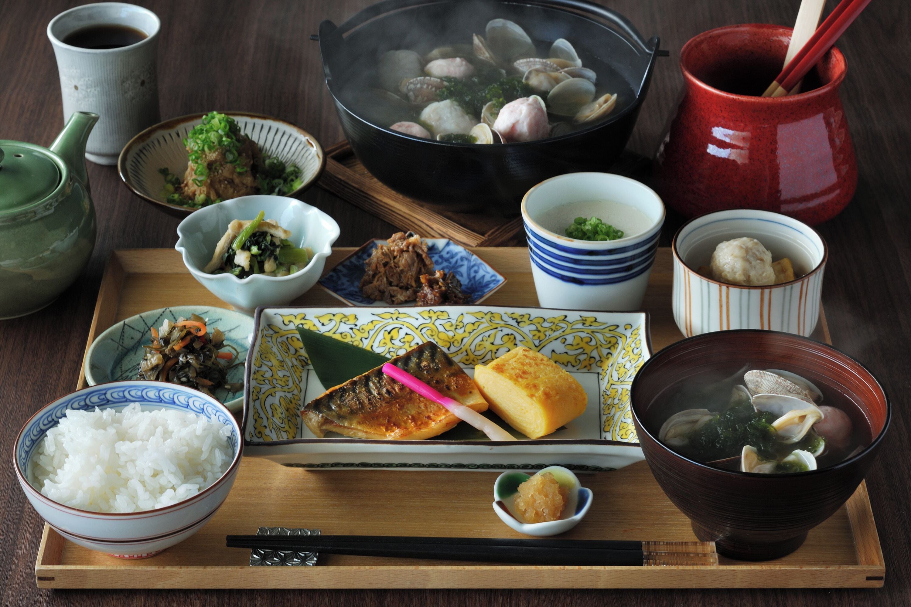 A variety of Japanese dishes on a wooden tray, including rice, fish, and soup.