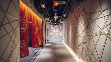 Un pasillo con paredes estampadas y cortinas rojas colgantes, que conduce a una habitación con techo de diseño geométrico.