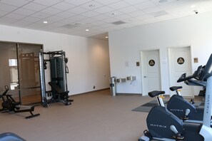 Een fitnessruimte met cardioapparatuur, krachtapparaten en een spiegelwand.