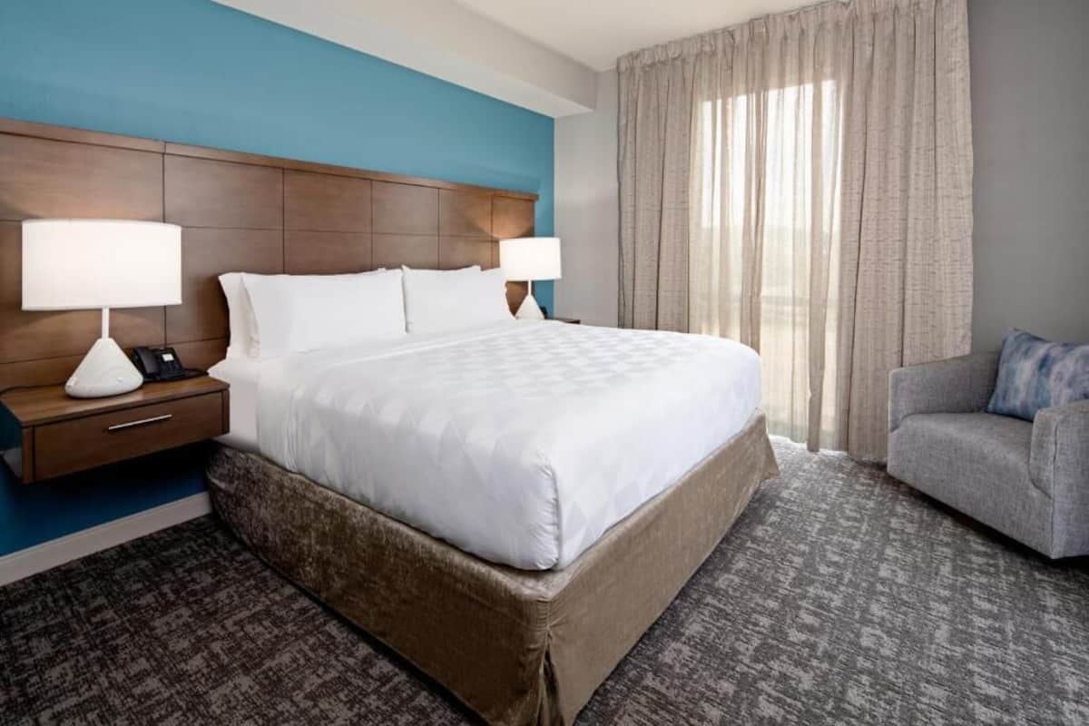 Quarto de hotel com uma cama grande, duas mesas de cabeceira com abajures, um sofá e vista para o exterior.